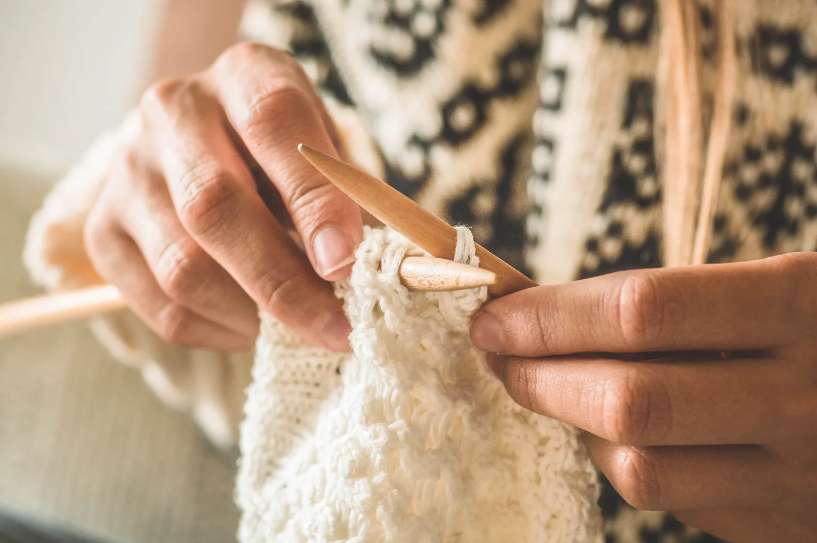 Close-up of hands knitting with light-colored yarn, slow and steady rhythm