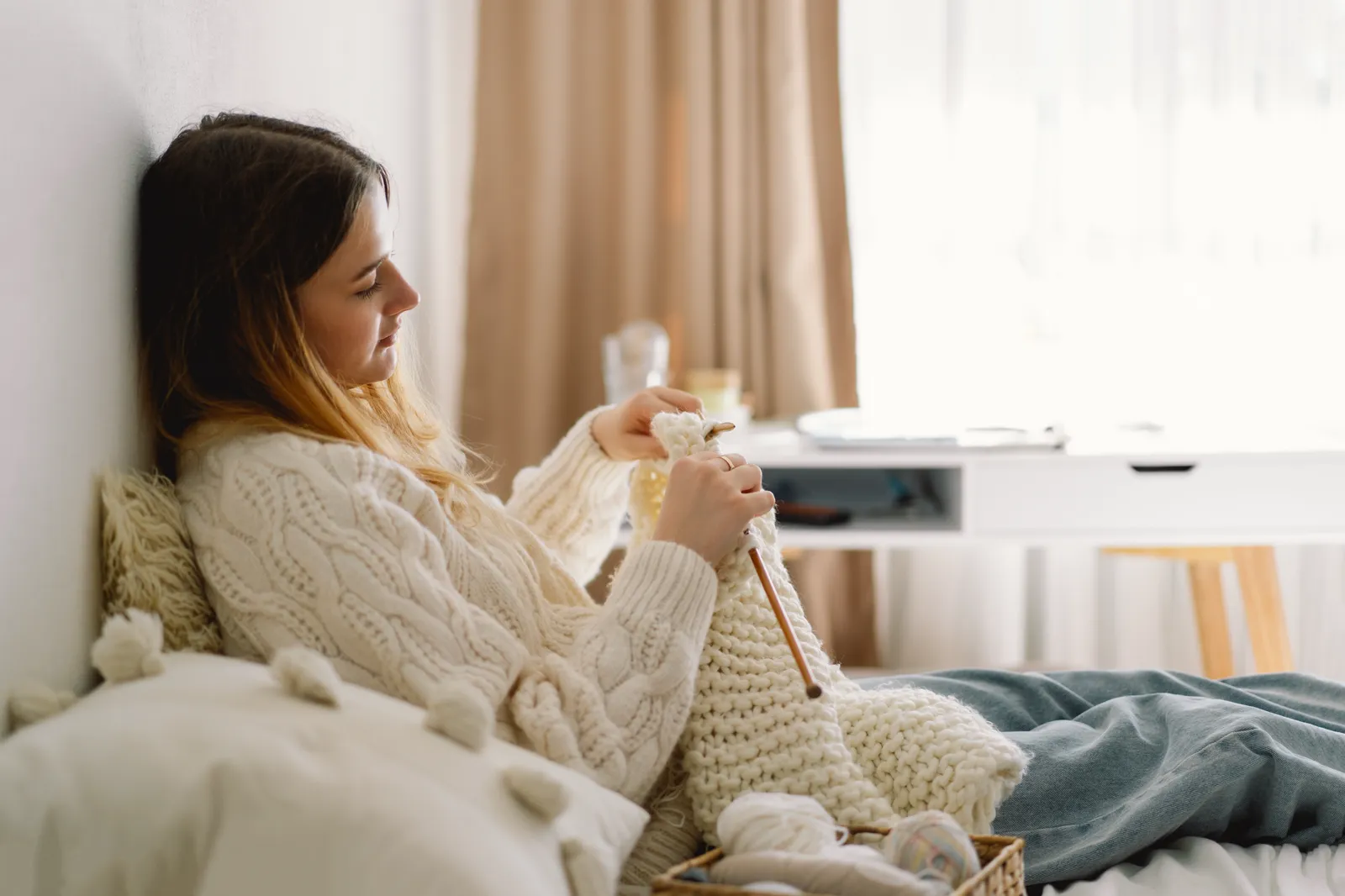 A woman knitting in soft natural light, cozy bedroom setting, mid-afternoon