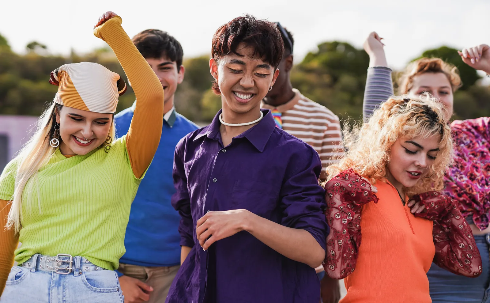 A group of teenagers laughing and celebrating together outdoors in colorful clothes