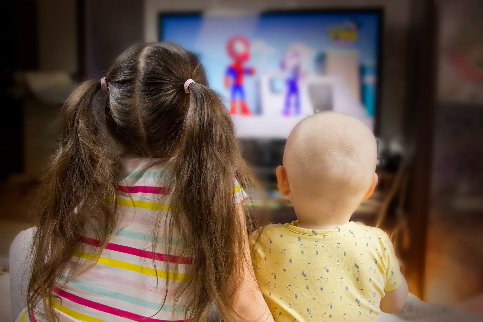 A family of two parents and a child sitting close together on a couch watching a screen, snacks within reach