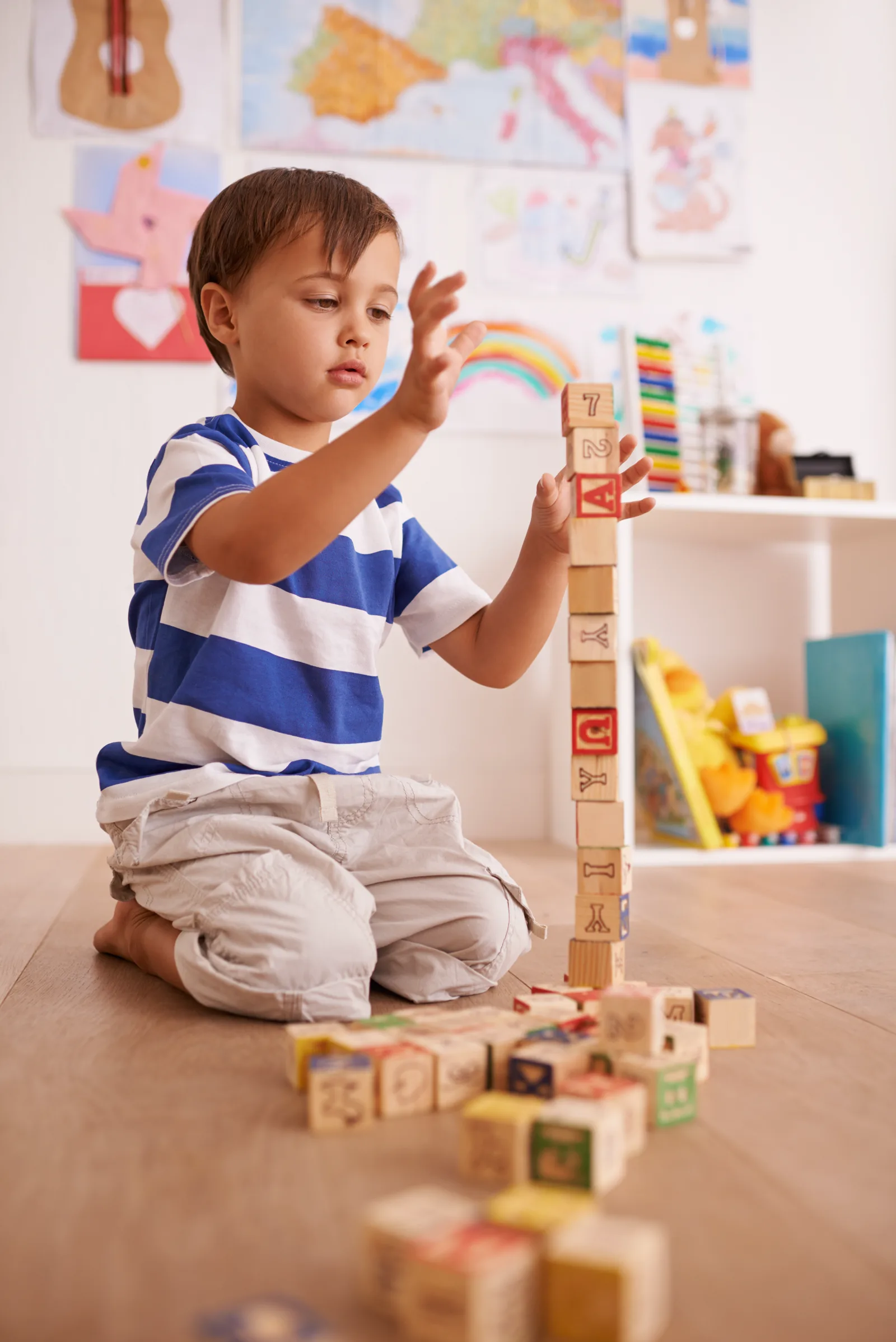 A young child sitting on the floor playing intently with colorful alphabet blocks indoors