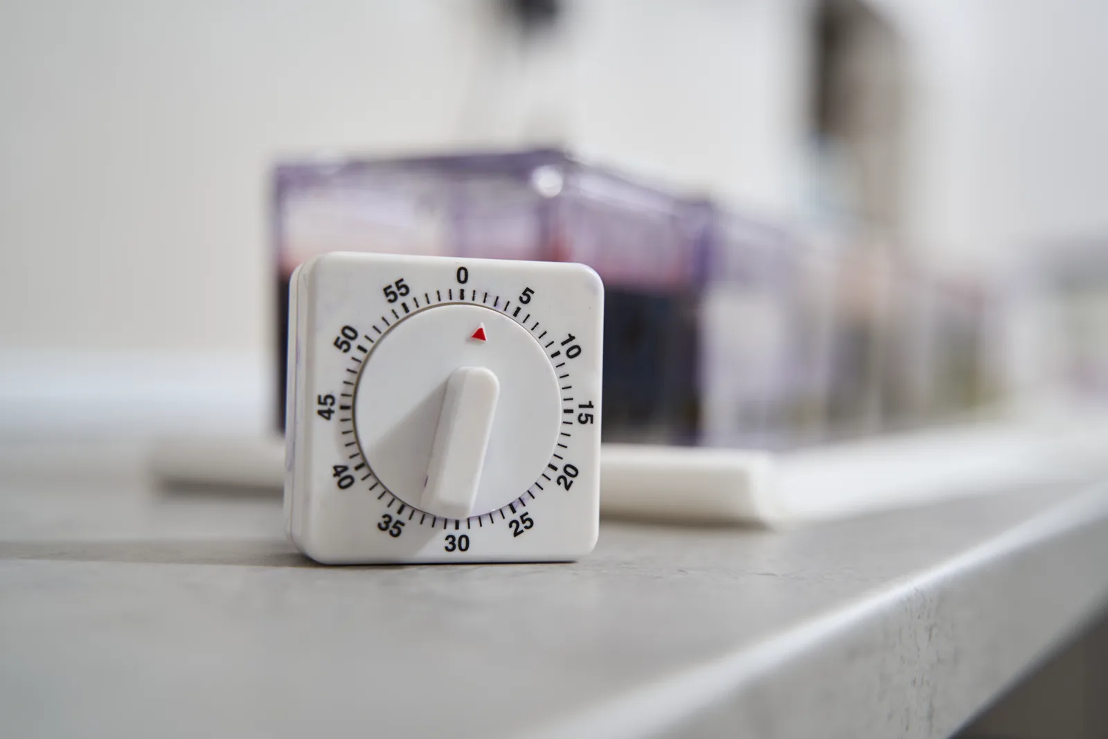 A simple white mechanical kitchen timer sitting on a grey countertop