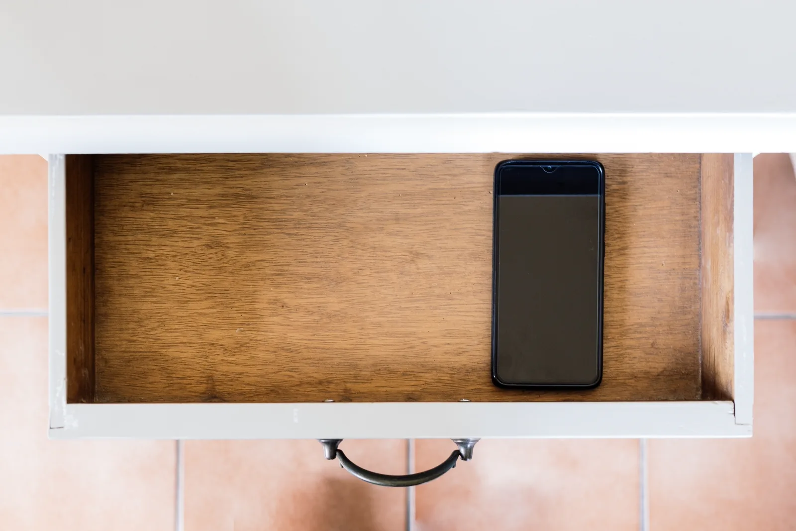 A smartphone face-down inside an open wooden drawer at home, the rest of the room out of focus