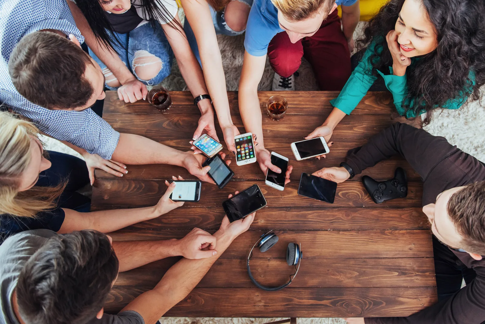 Top-down view of several pairs of hands around a cafe table, each holding a smartphone, drinks scattered between them
