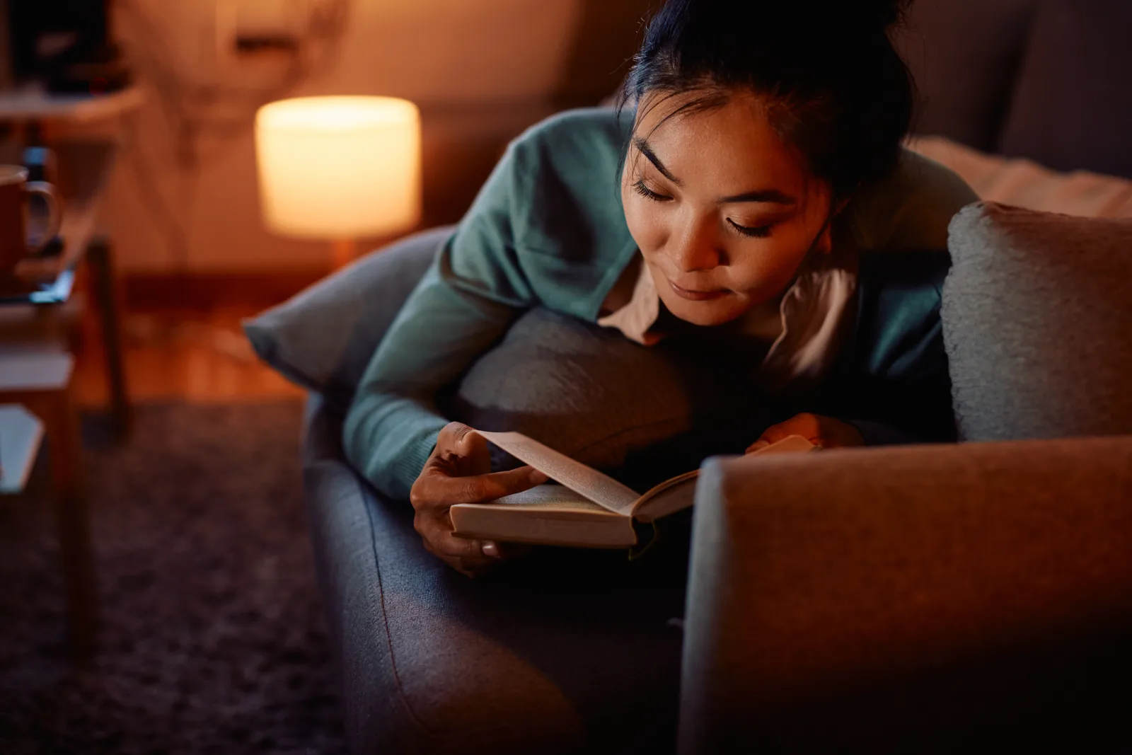 A relaxed woman reading a paper book at home, soft natural light, no screens visible