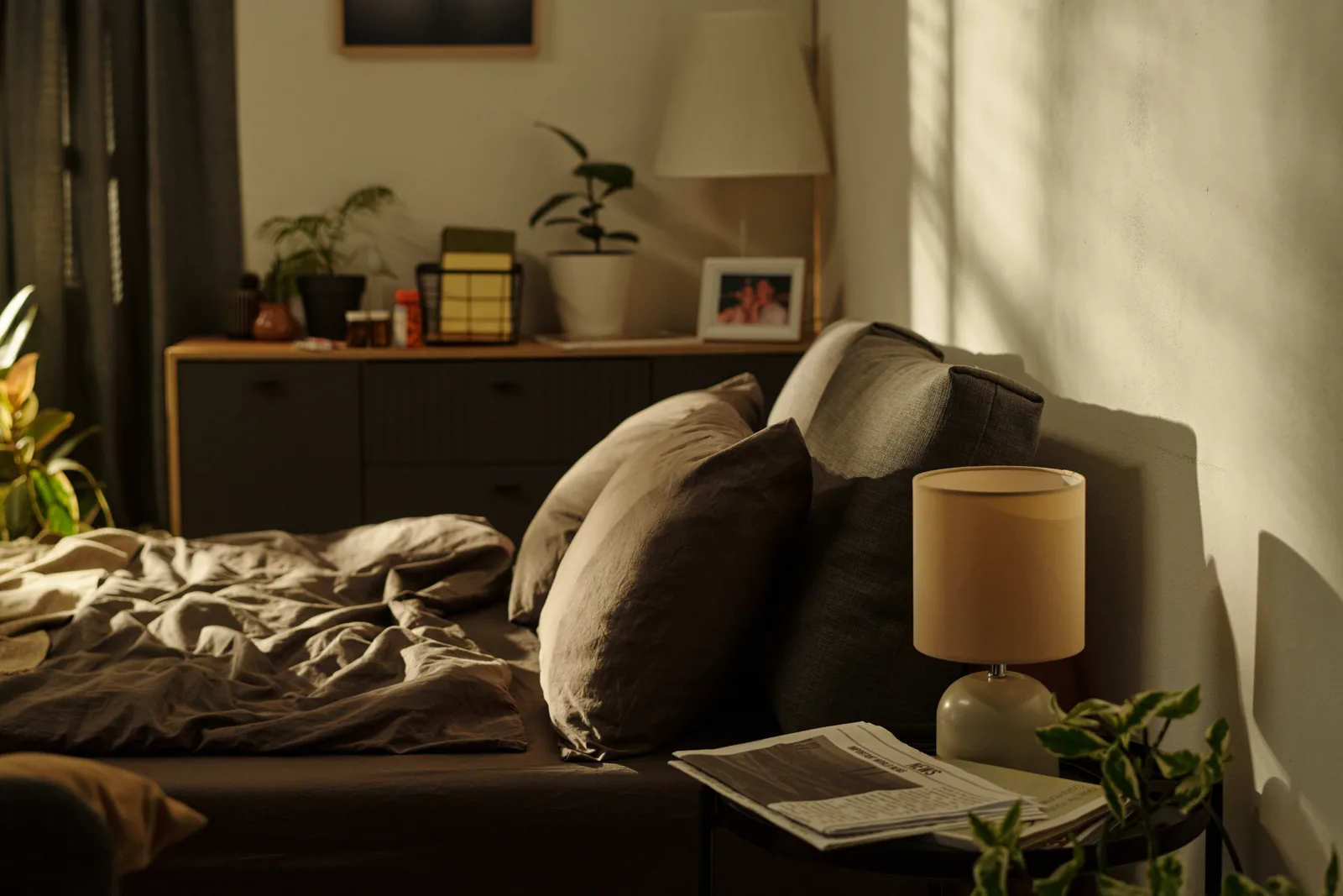 A calm dimly lit bedroom with a paper book and a small lamp on the nightstand, no phone in sight, warm evening light