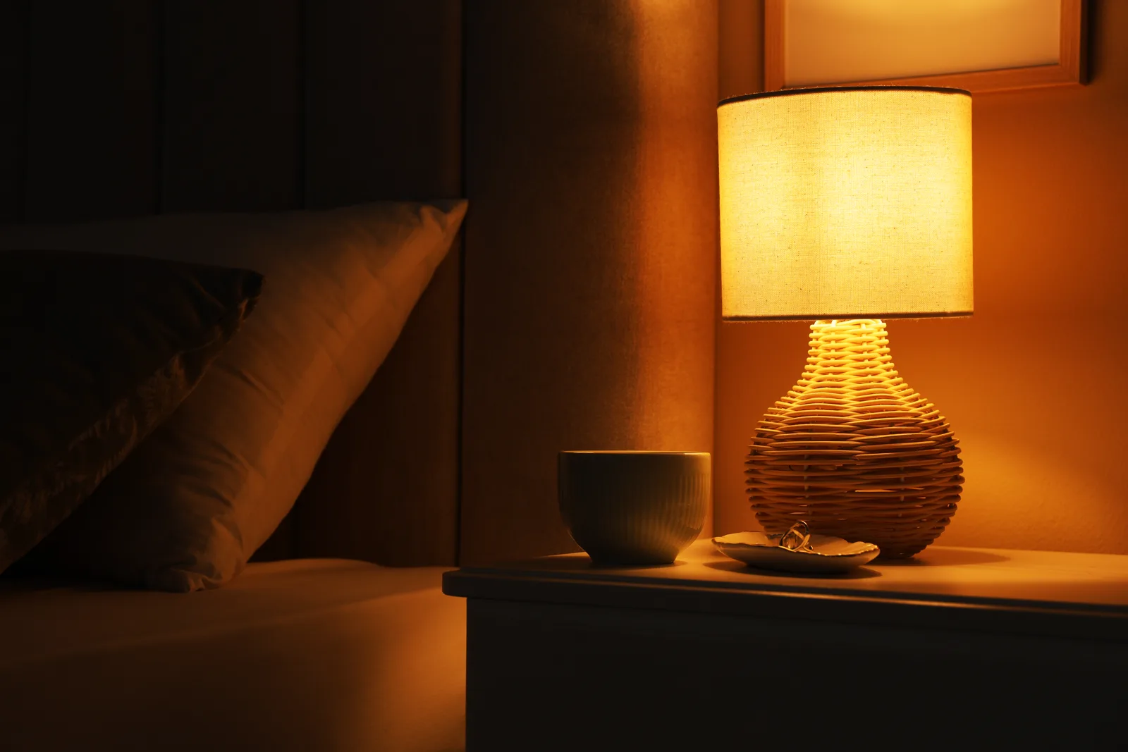 A warm glowing bedside lamp on a nightstand in a cozy dark bedroom, soft amber light