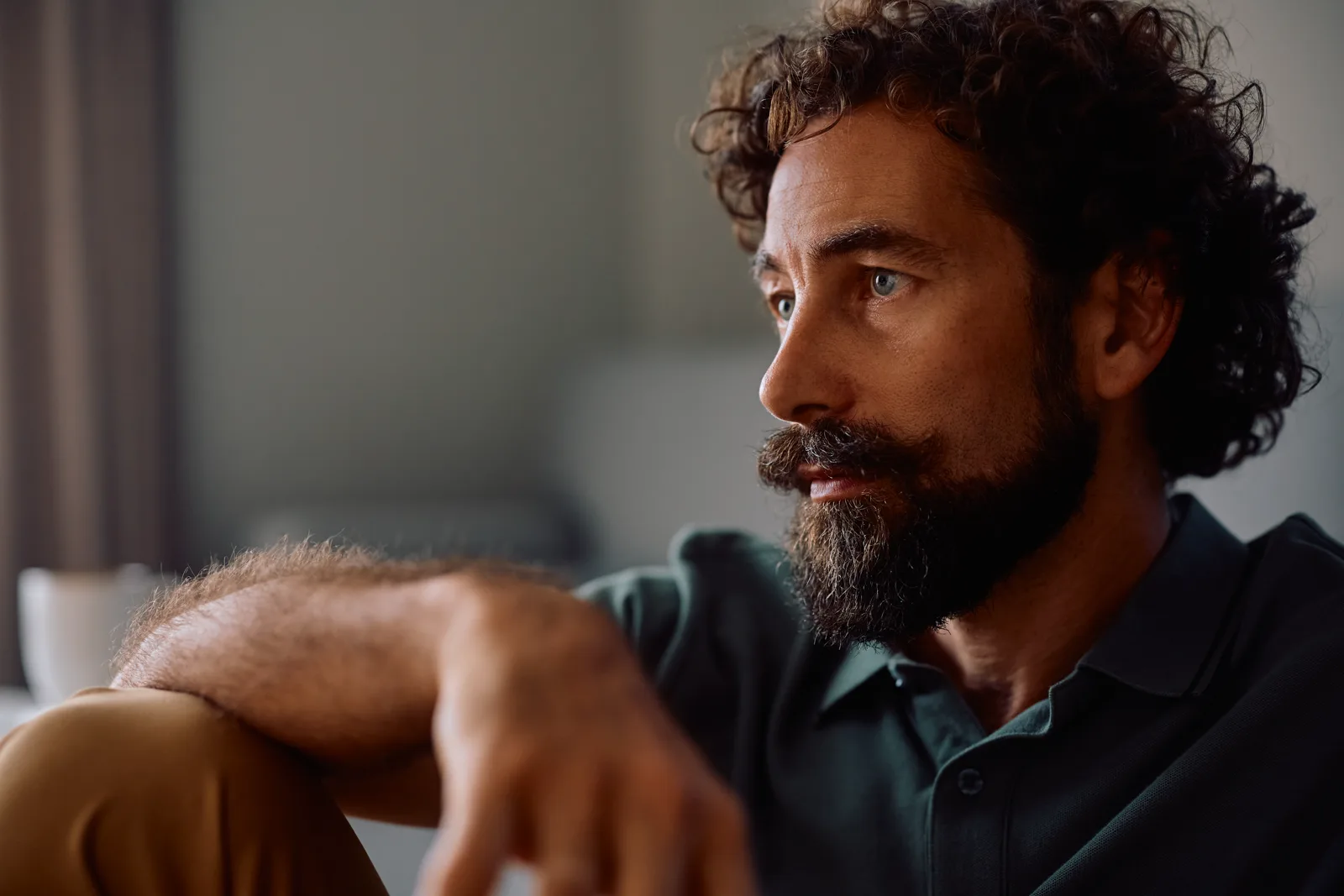 A contemplative man with curly hair looking off to the side, calm and reflective in soft natural light