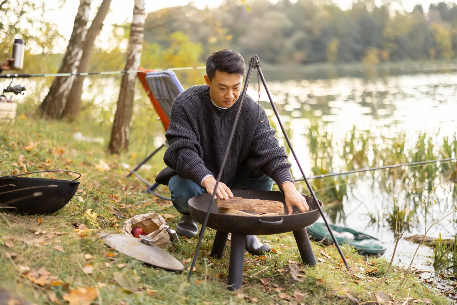 A man tending a charcoal grill outdoors, smoke rising, evening light