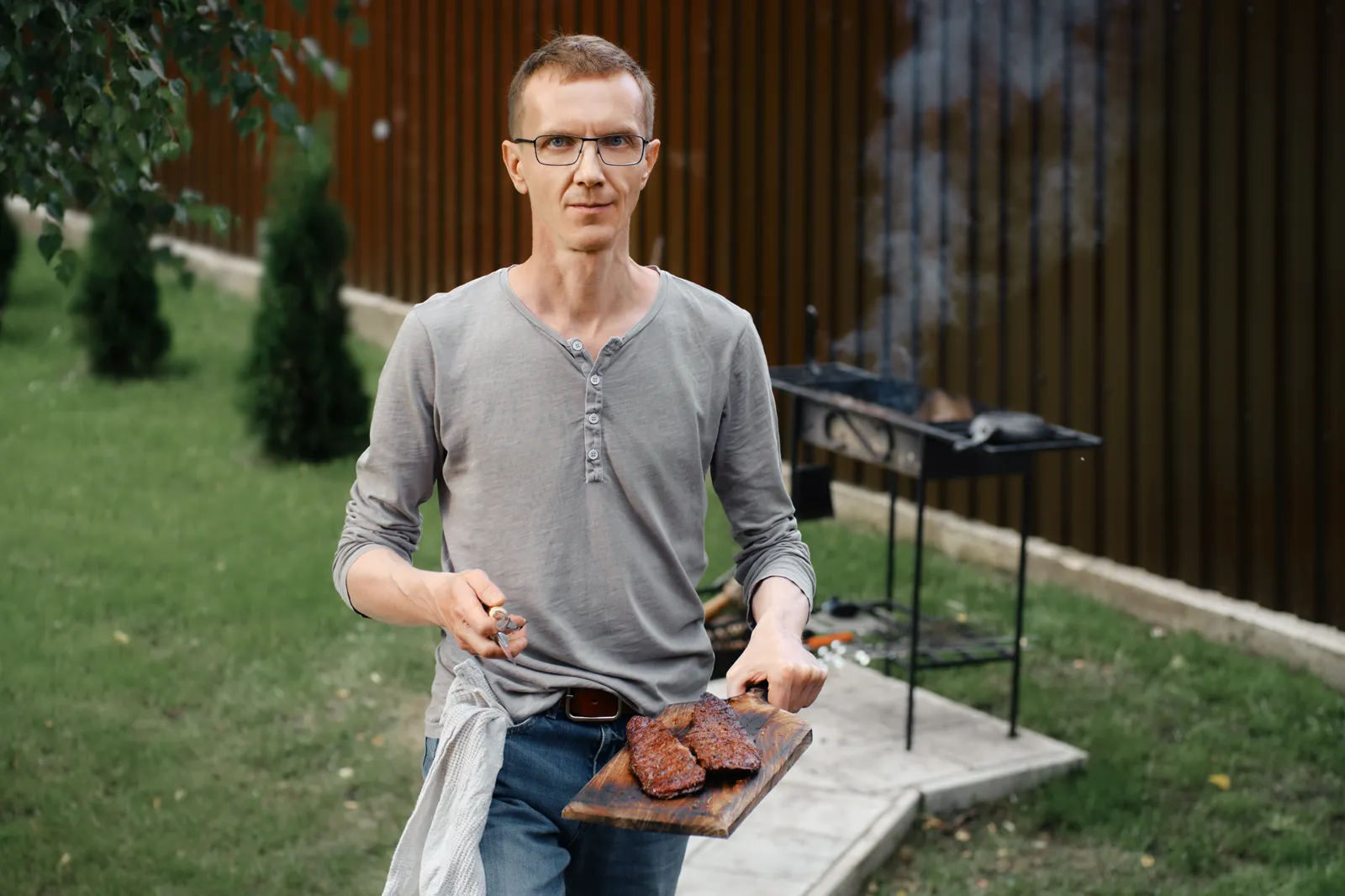A satisfied man carrying a steak fresh off the grill, casual clothes, end of cooking