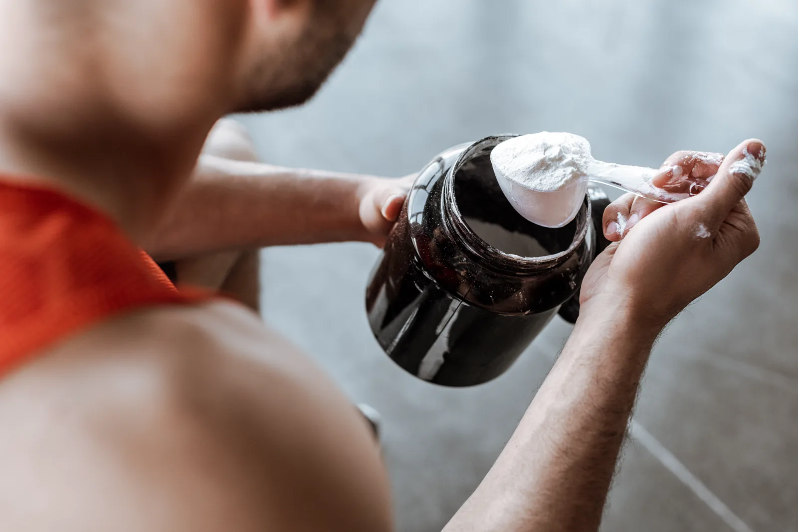 A close-up of a person scooping pre-workout powder from a jar with a measuring scoop