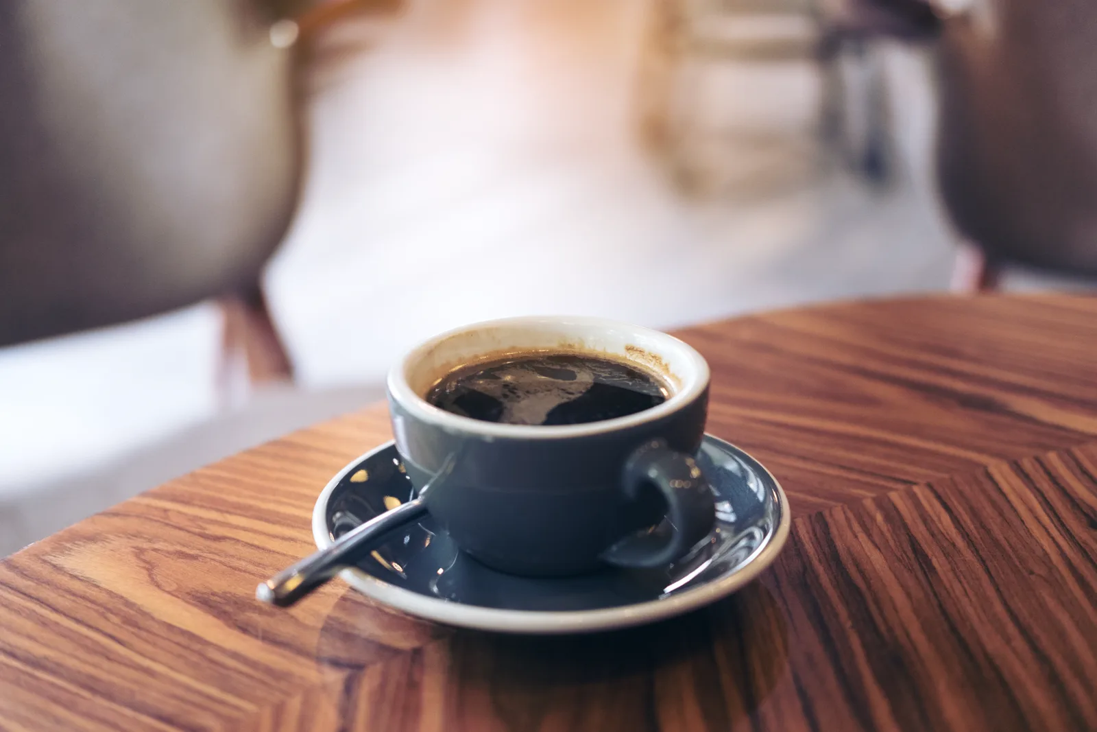 A close-up of a hot Americano coffee cup on a vintage wooden table in warm morning light