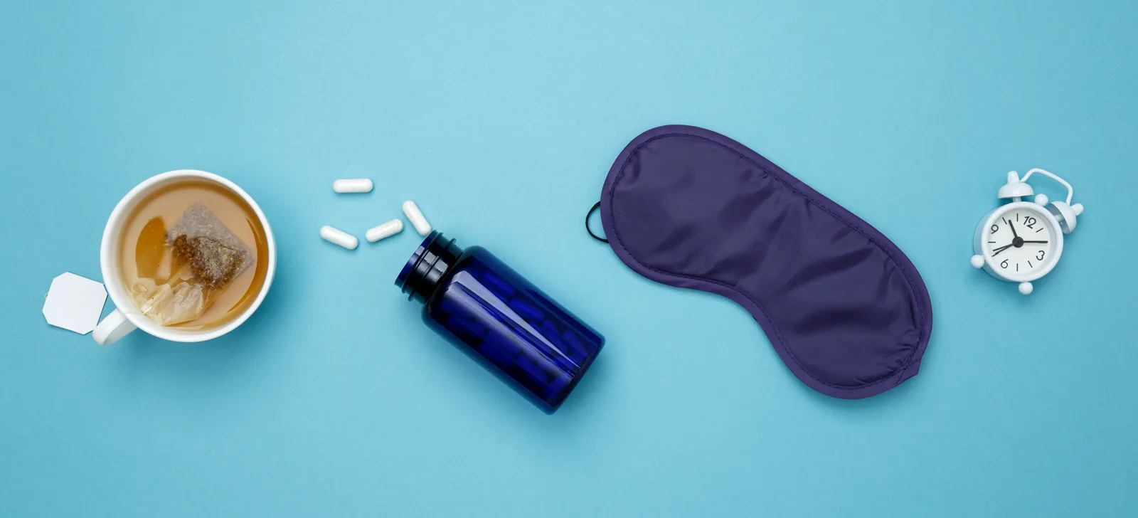 A calm nighttime routine on a bedside table, a warm cup of tea next to a small bottle of sleep aids in soft lamplight