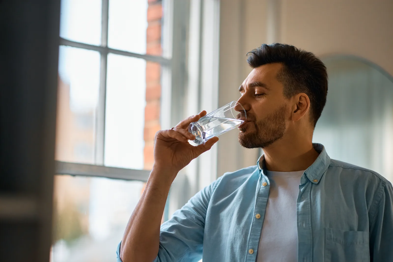 A man drinking a glass of fresh water in a bright home kitchen, calm everyday moment
