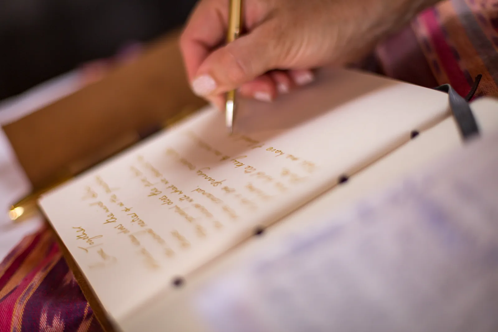 A close-up of a hand writing in an open book or notebook in soft warm light