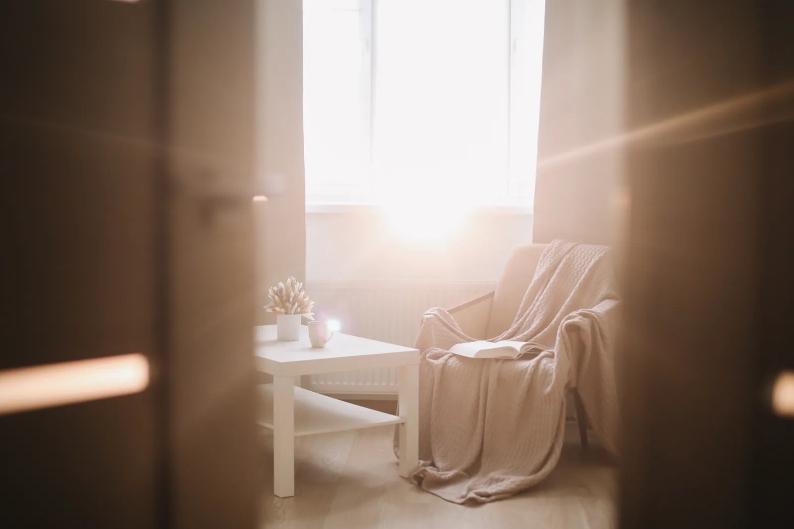A cozy chair with a blanket and an open book bathed in warm sunlight by a window