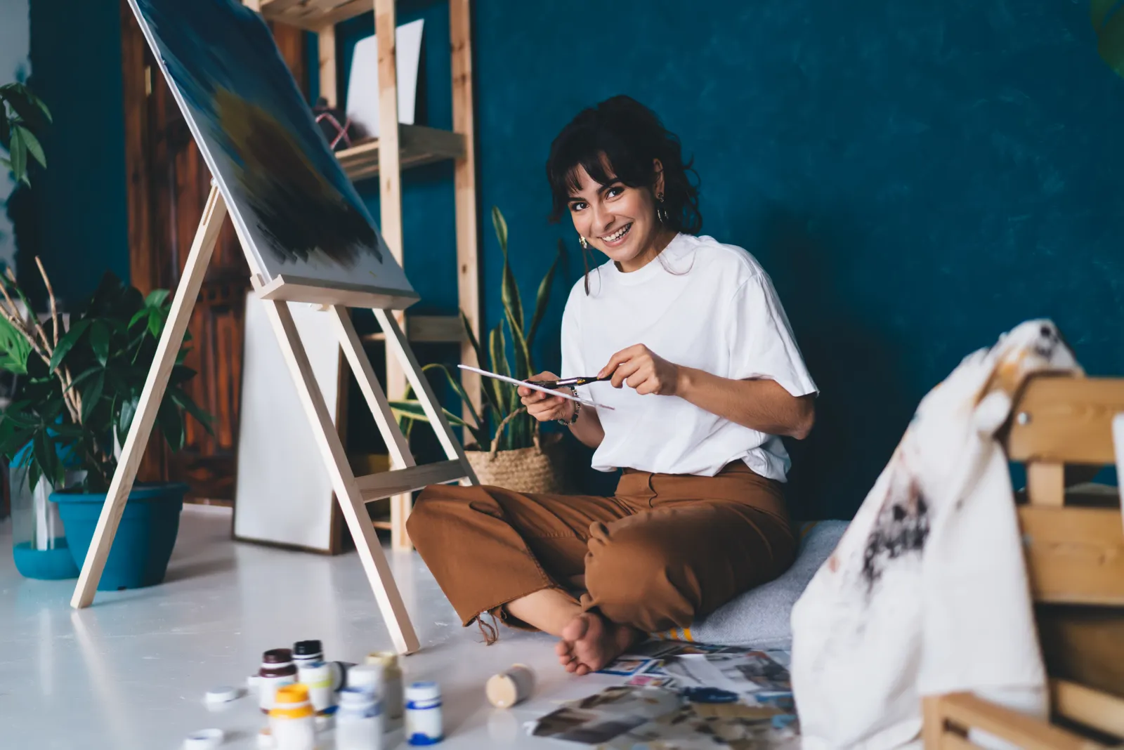 A woman smiling while painting in her art studio, sunlight on the canvas