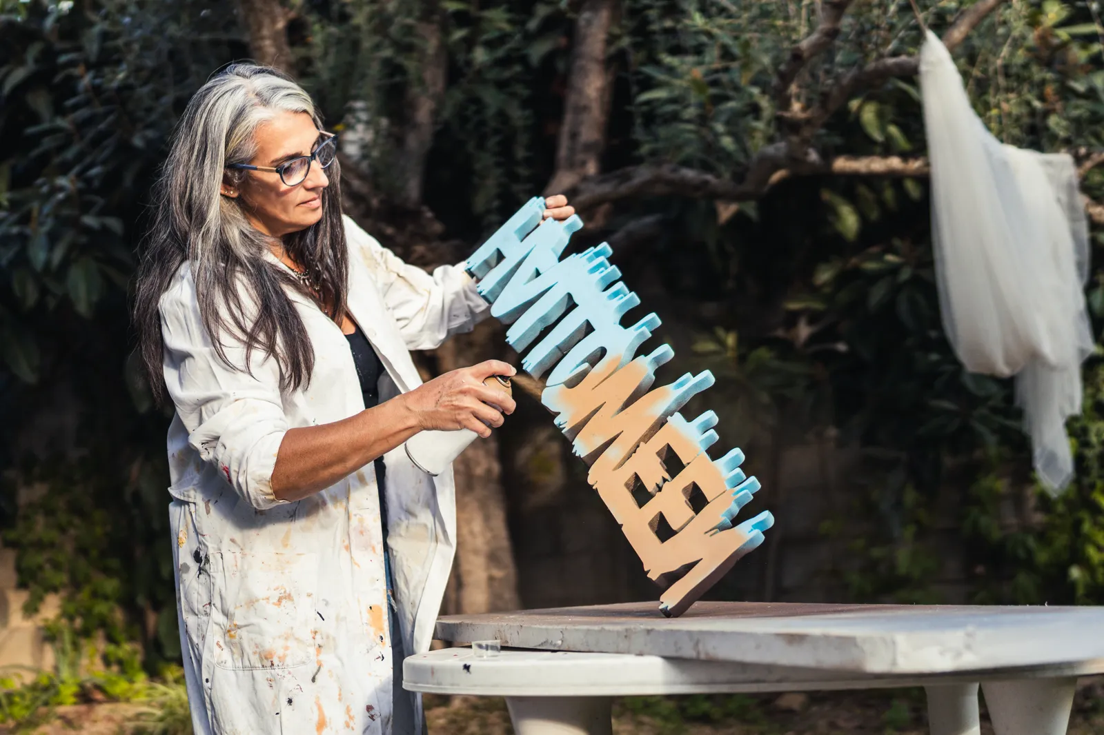 A woman with grey hair carefully painting some polystyrene letters, focused