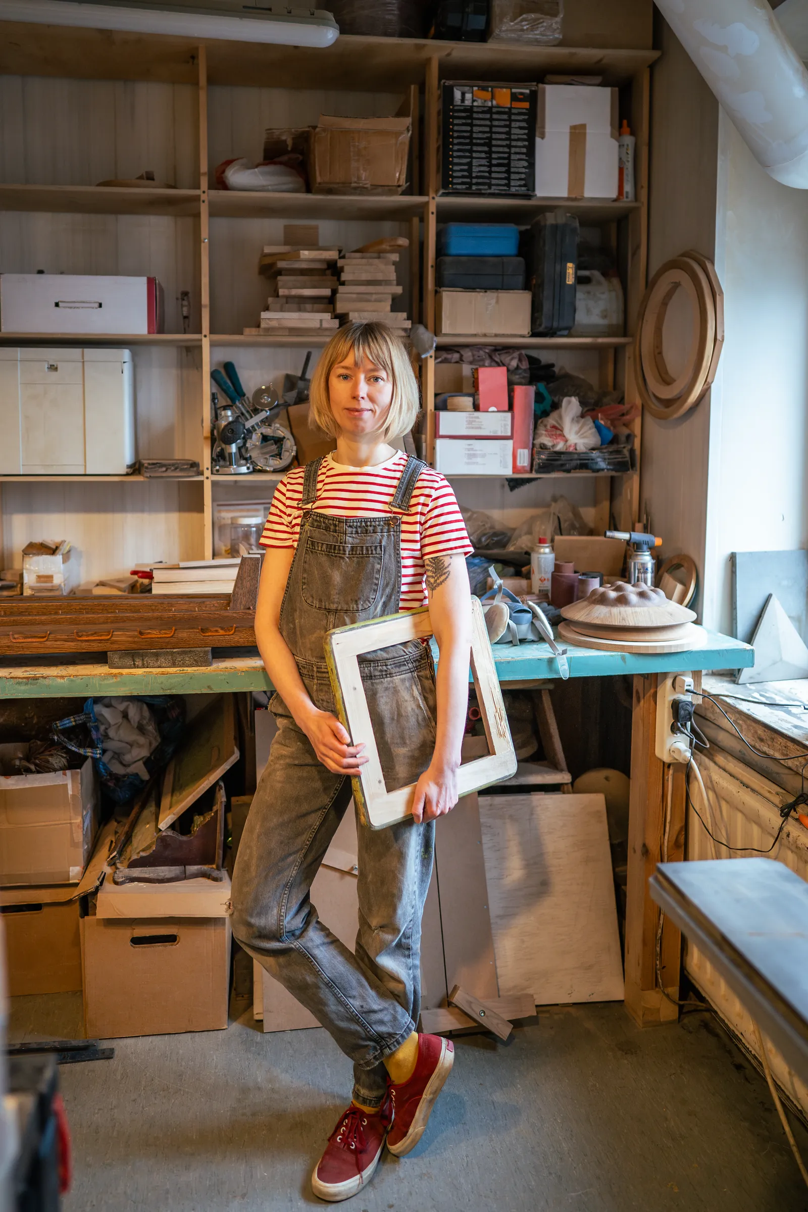 A relaxed thoughtful woman on a break from carpentry, holding something she's working on