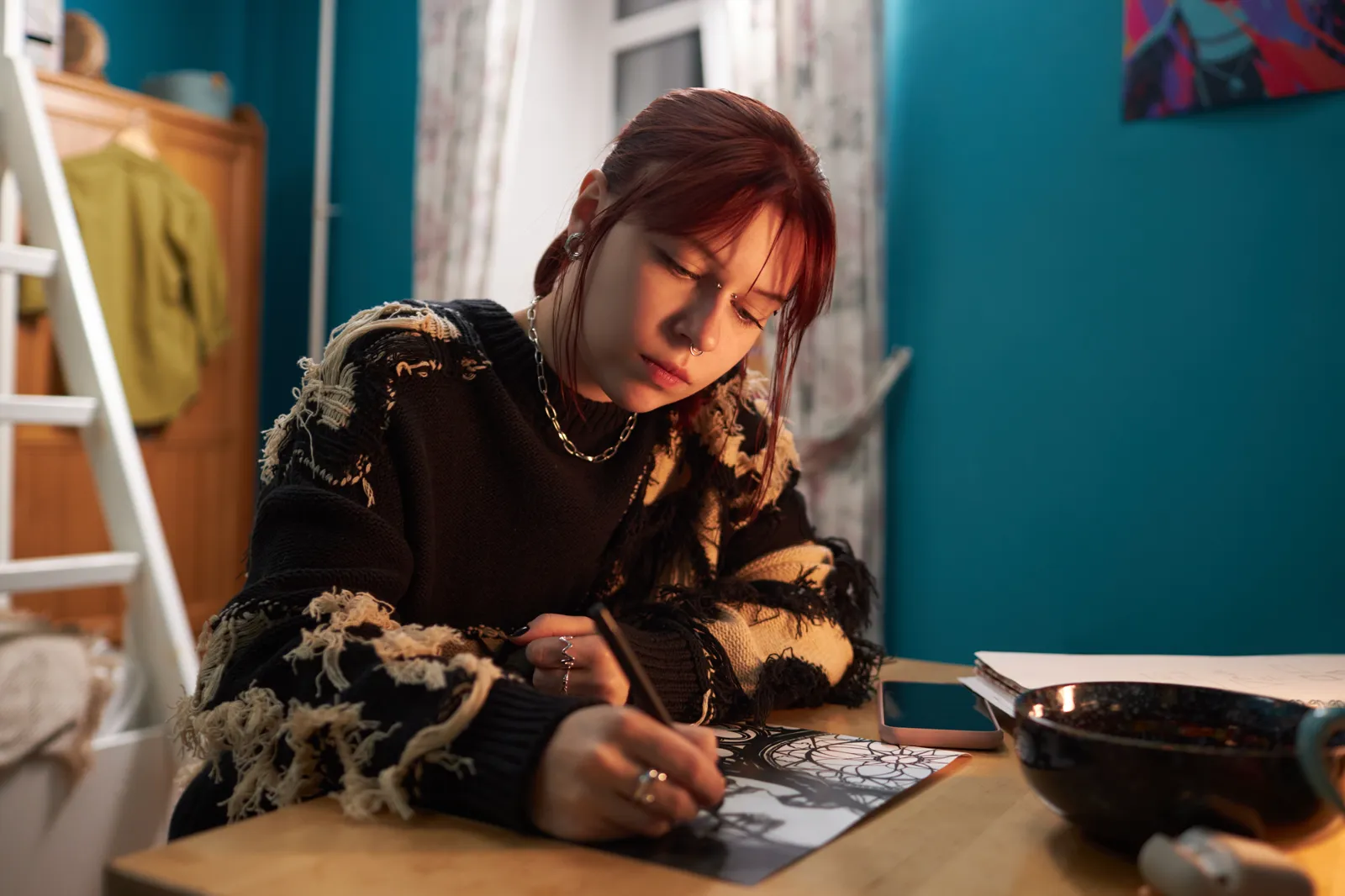 A young woman drawing in her room, focused and quiet, soft afternoon light