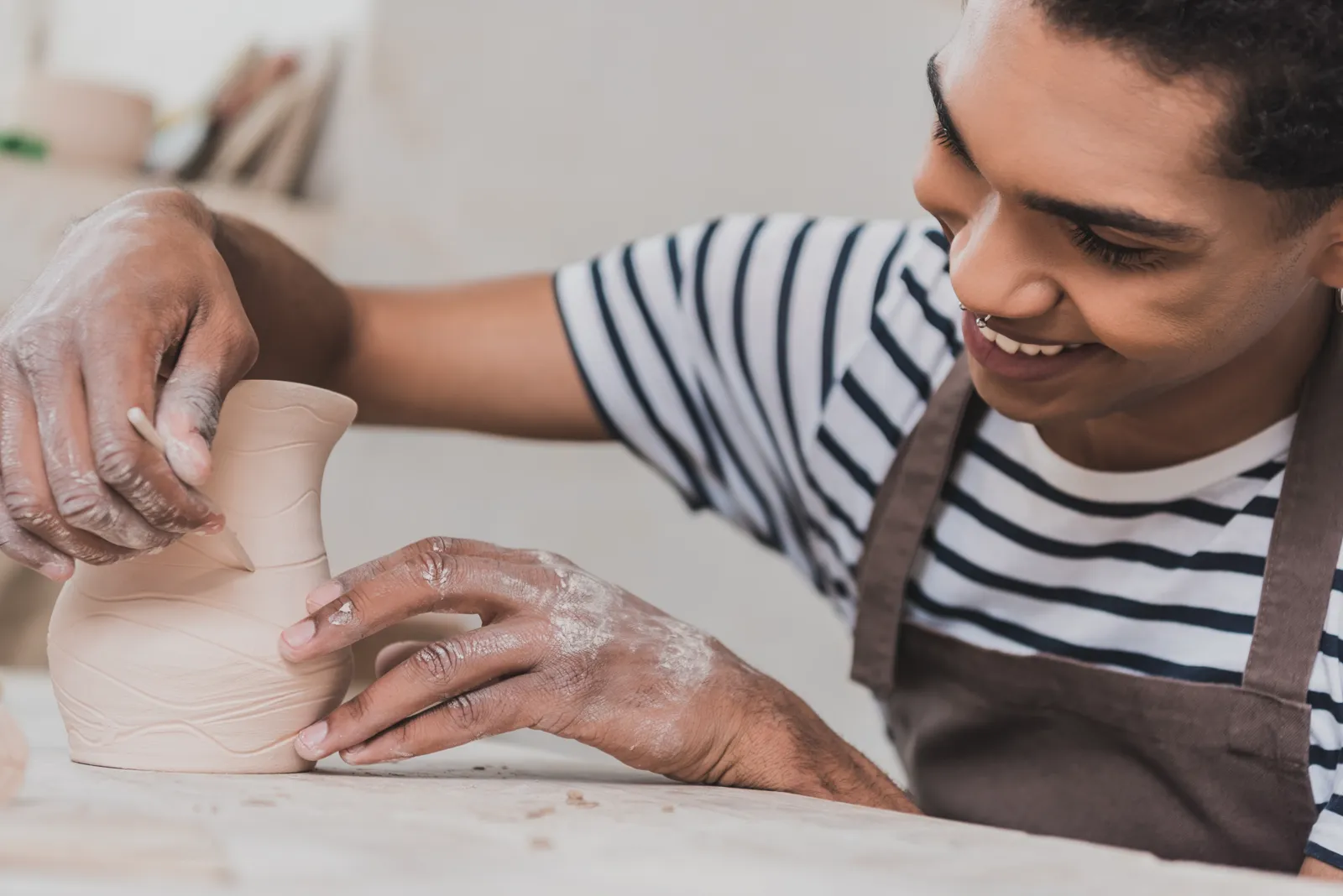 A cheerful man working on pottery in a small workshop, hands on the clay