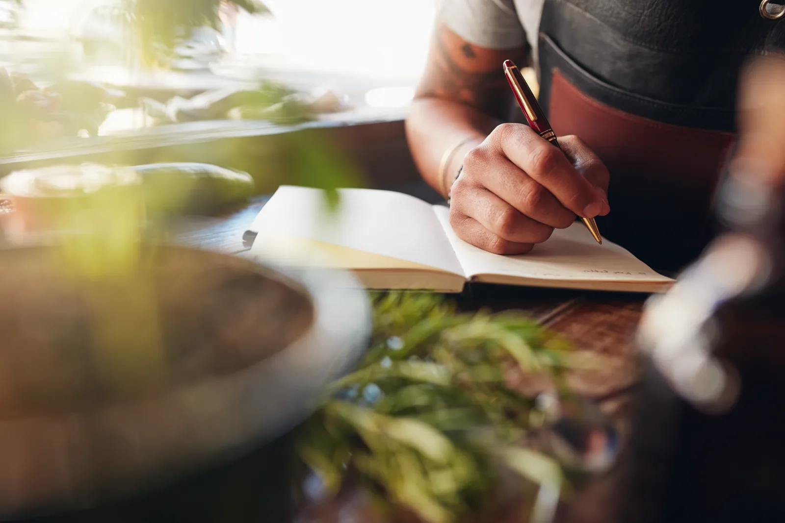 An open gratitude journal with a pen, a candle, and a warm drink on a wooden table