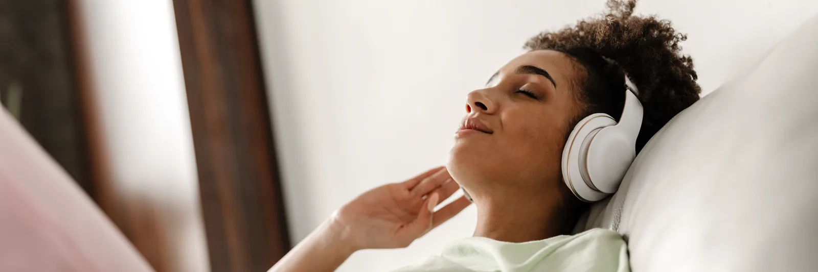 A person relaxing at home wearing headphones, eyes closed, warm light