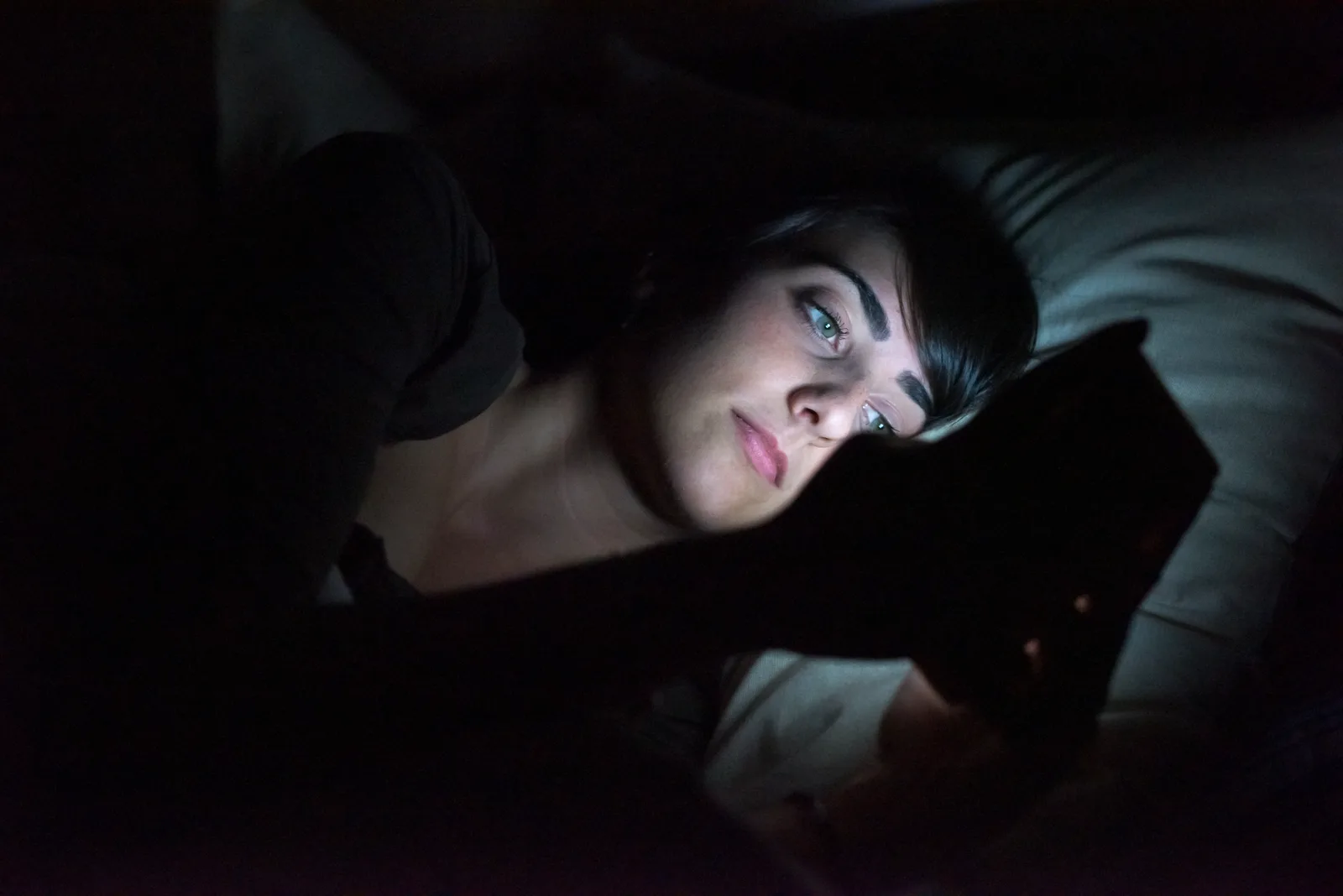 A woman scrolling on her phone in the dark, unable to put it down