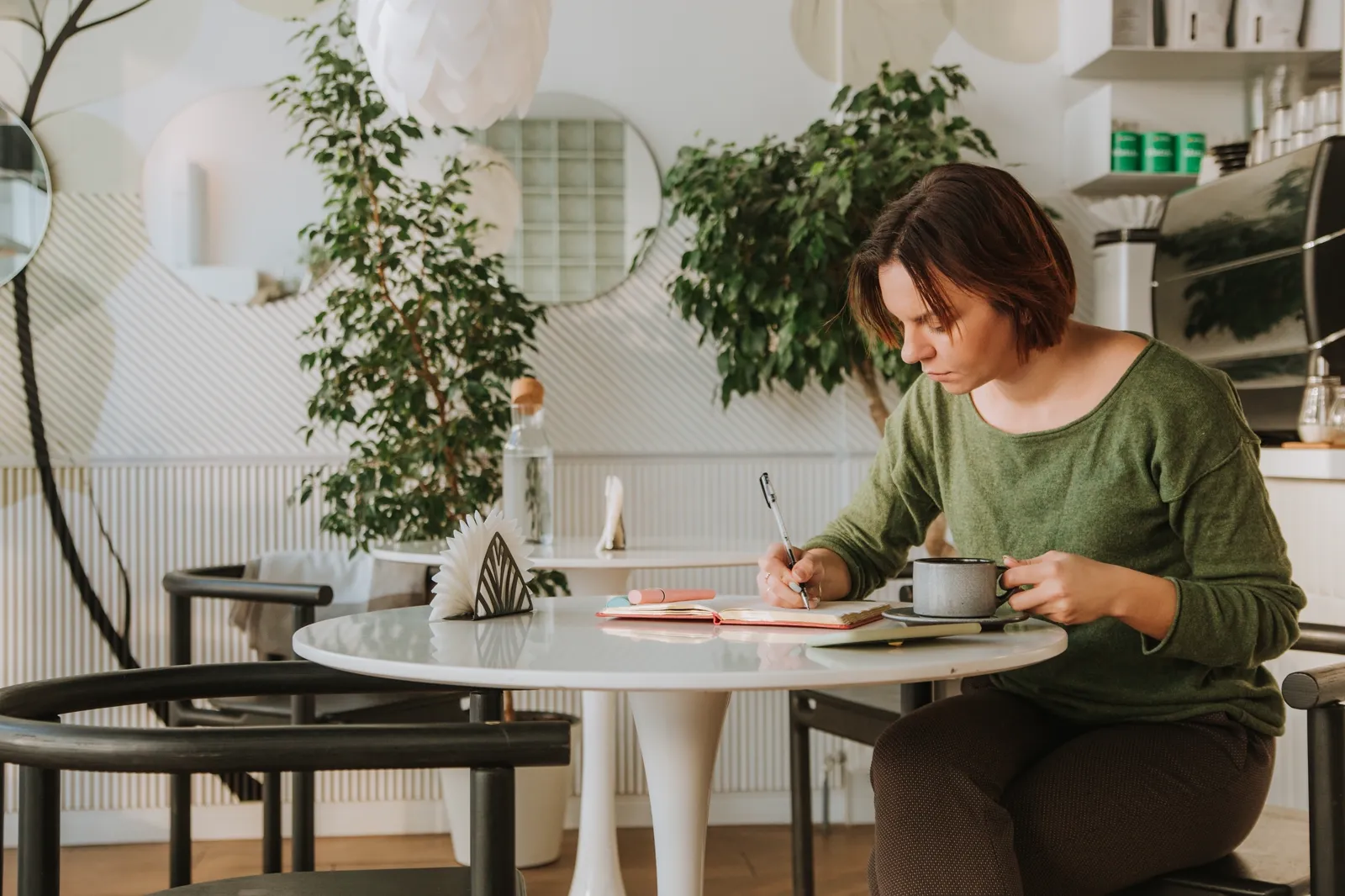 A young woman alone at a cafe table, calm posture, book and coffee in front of her