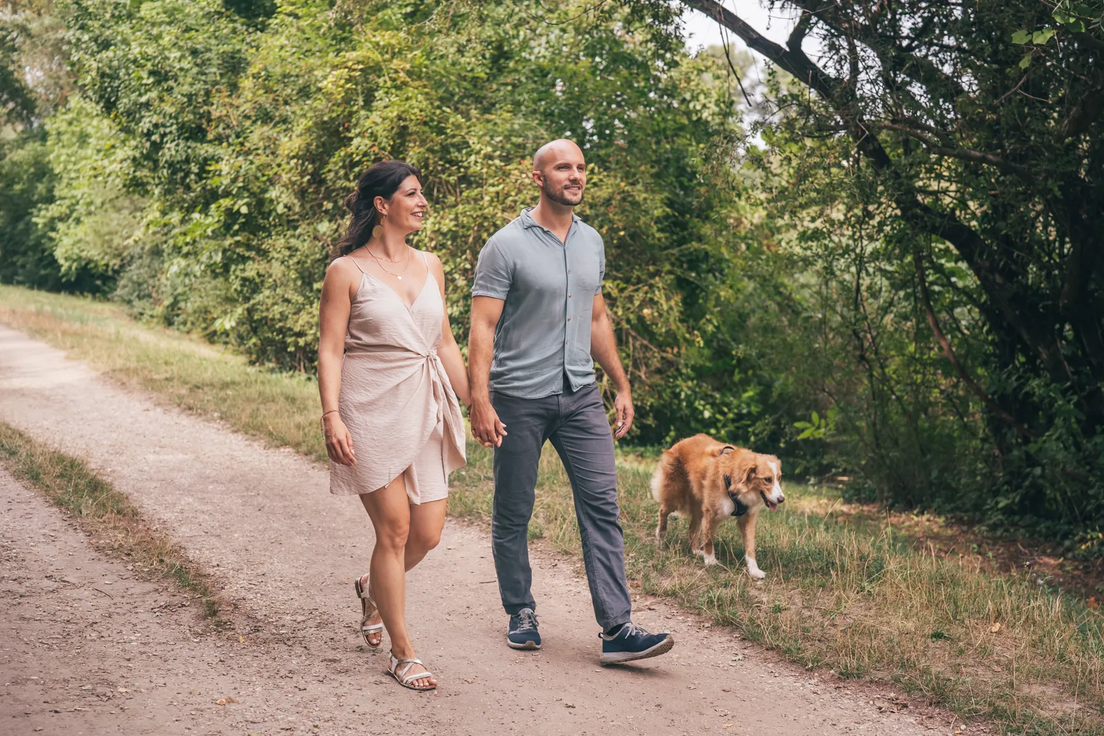 An affectionate couple strolling with their dog on a rural path in autumn