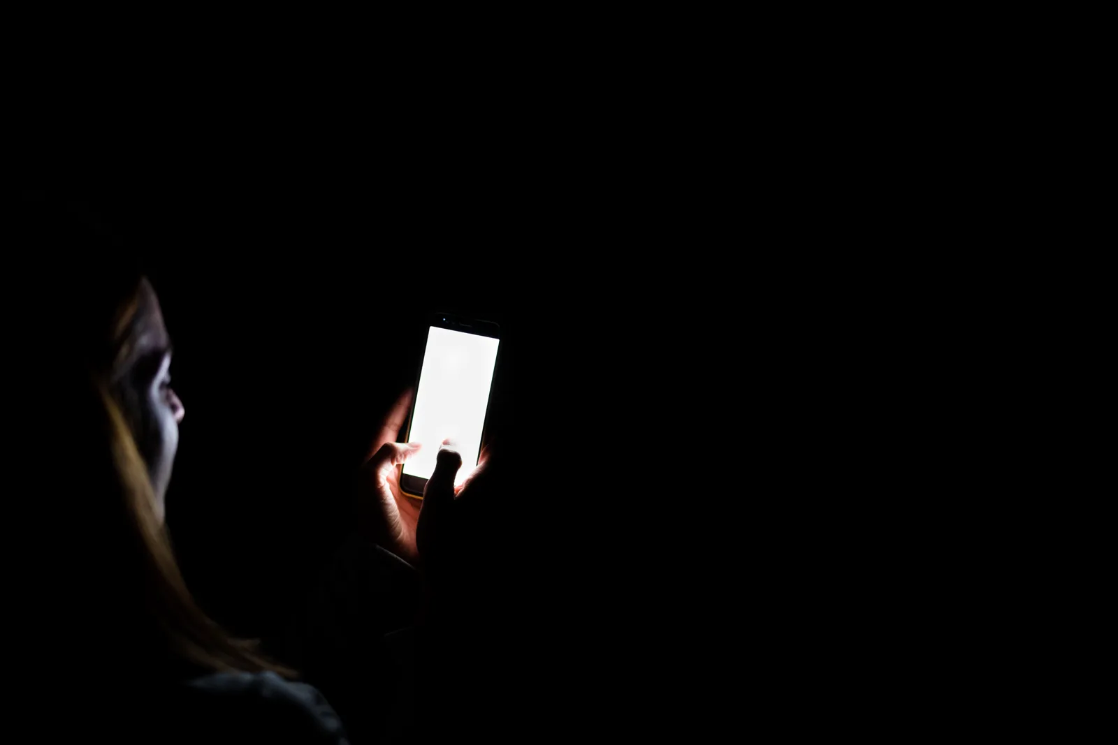 A face lit only by the glow of a phone screen in a dark bedroom late at night