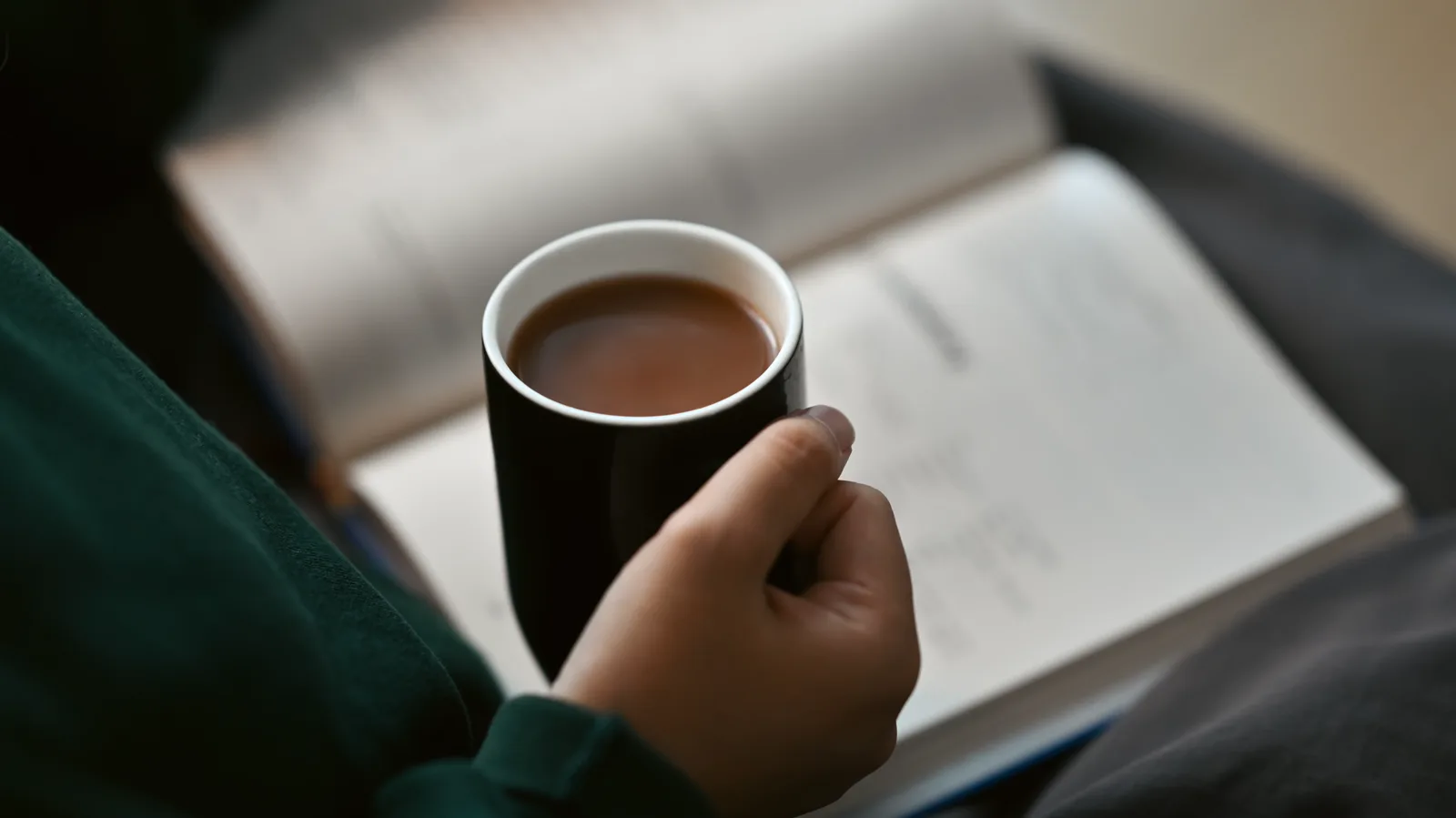 A person reading a paper book with a warm cup of coffee at home