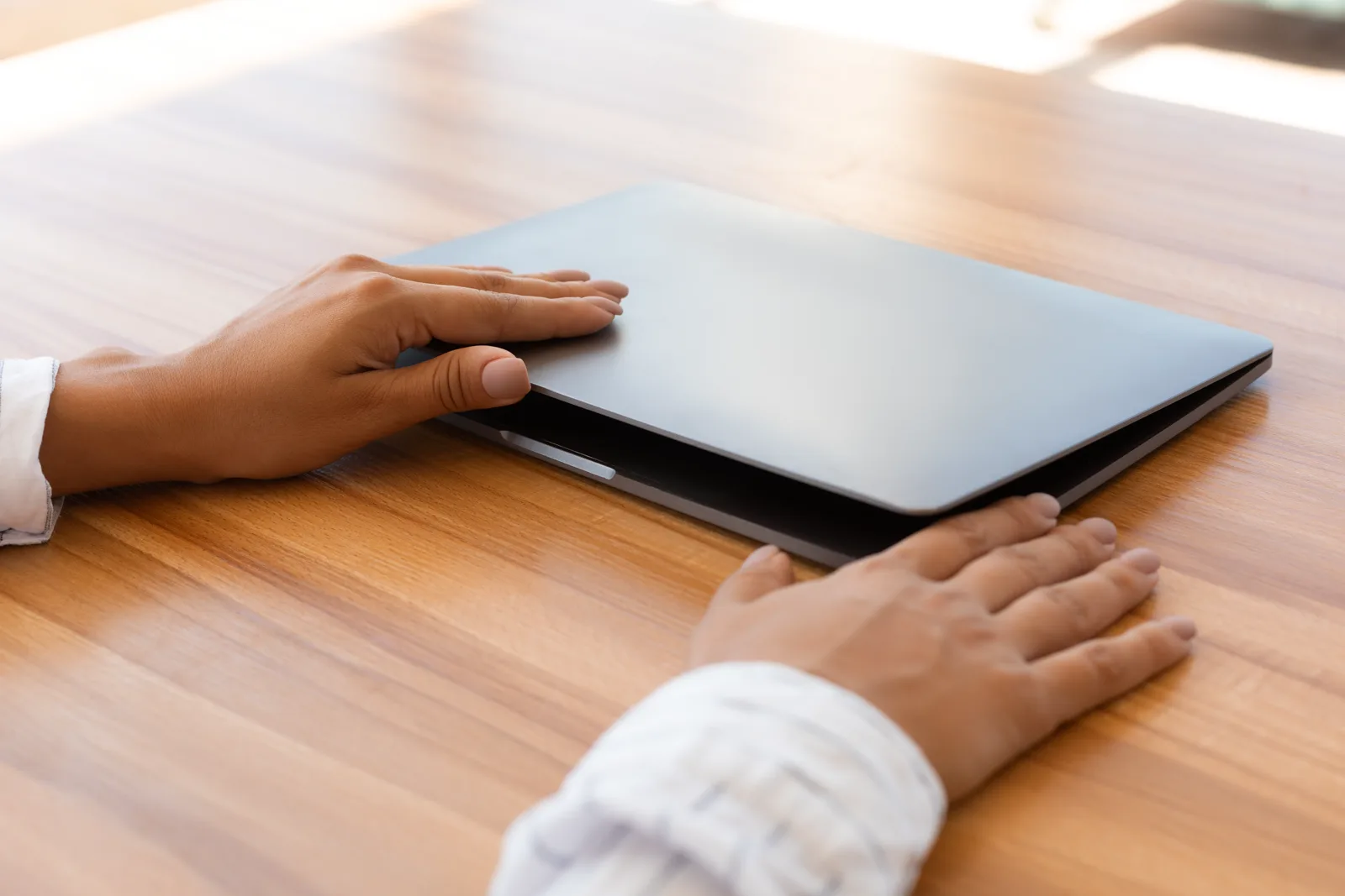 A pair of hands gently opening a laptop on a wooden desk, calm morning light