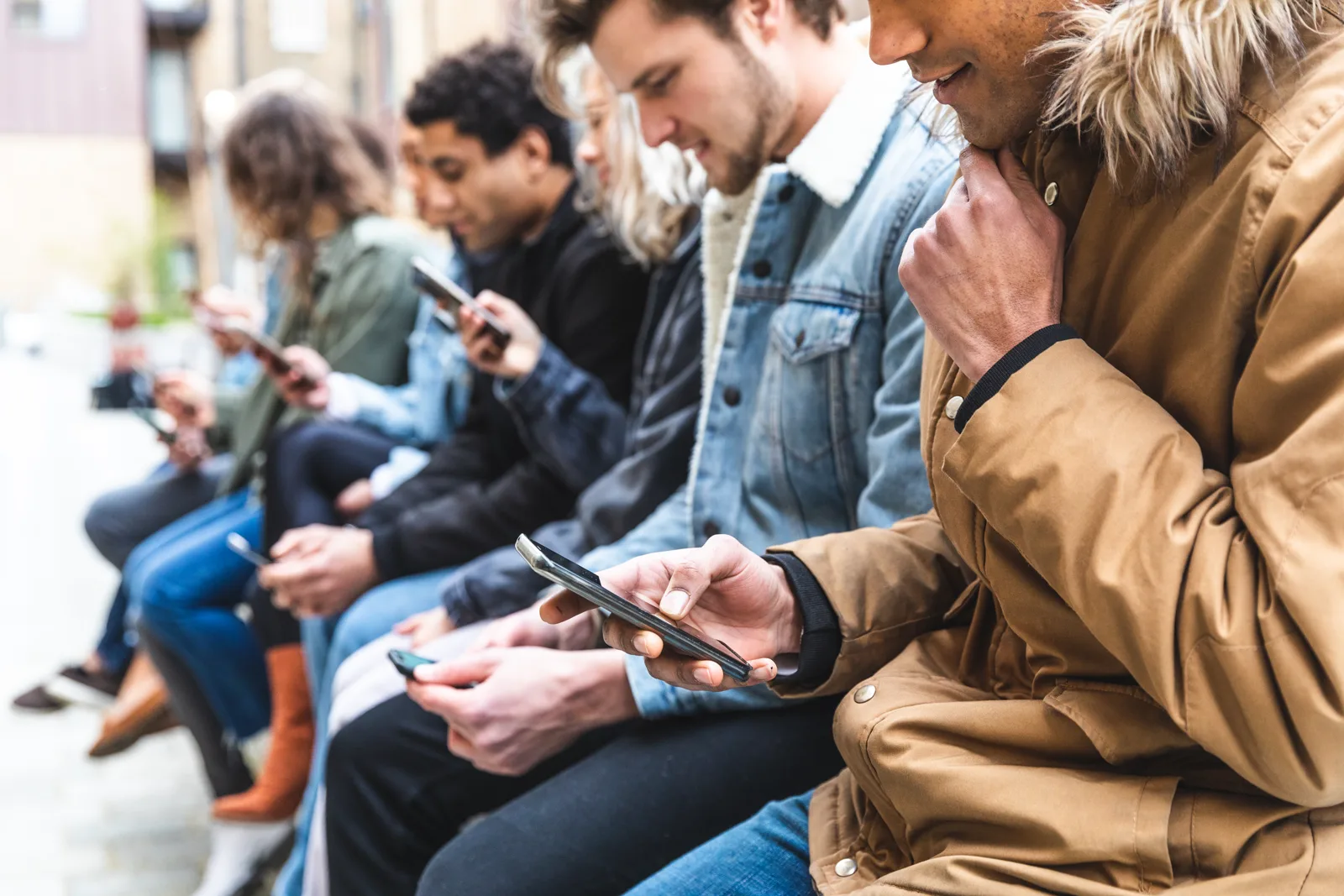 A multicultural group of friends sitting together but all looking at their separate smartphones