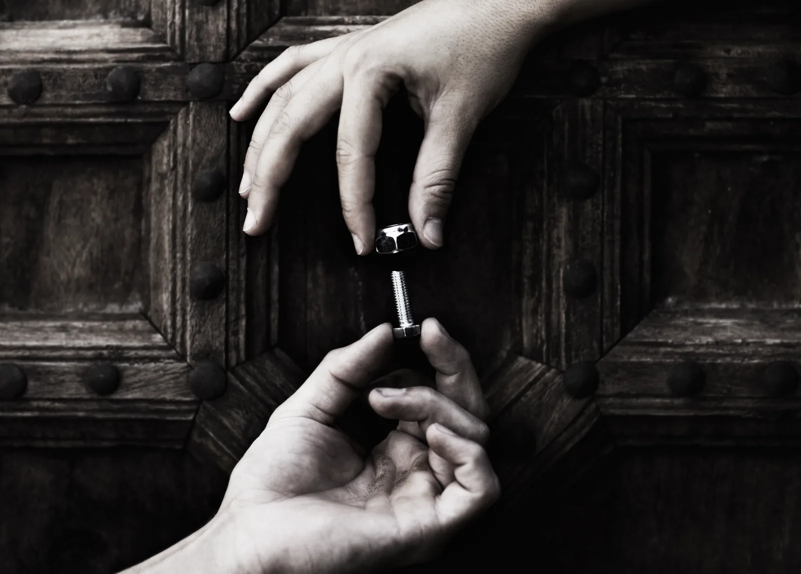Two hands fitting a nut and bolt together against a dark wood background
