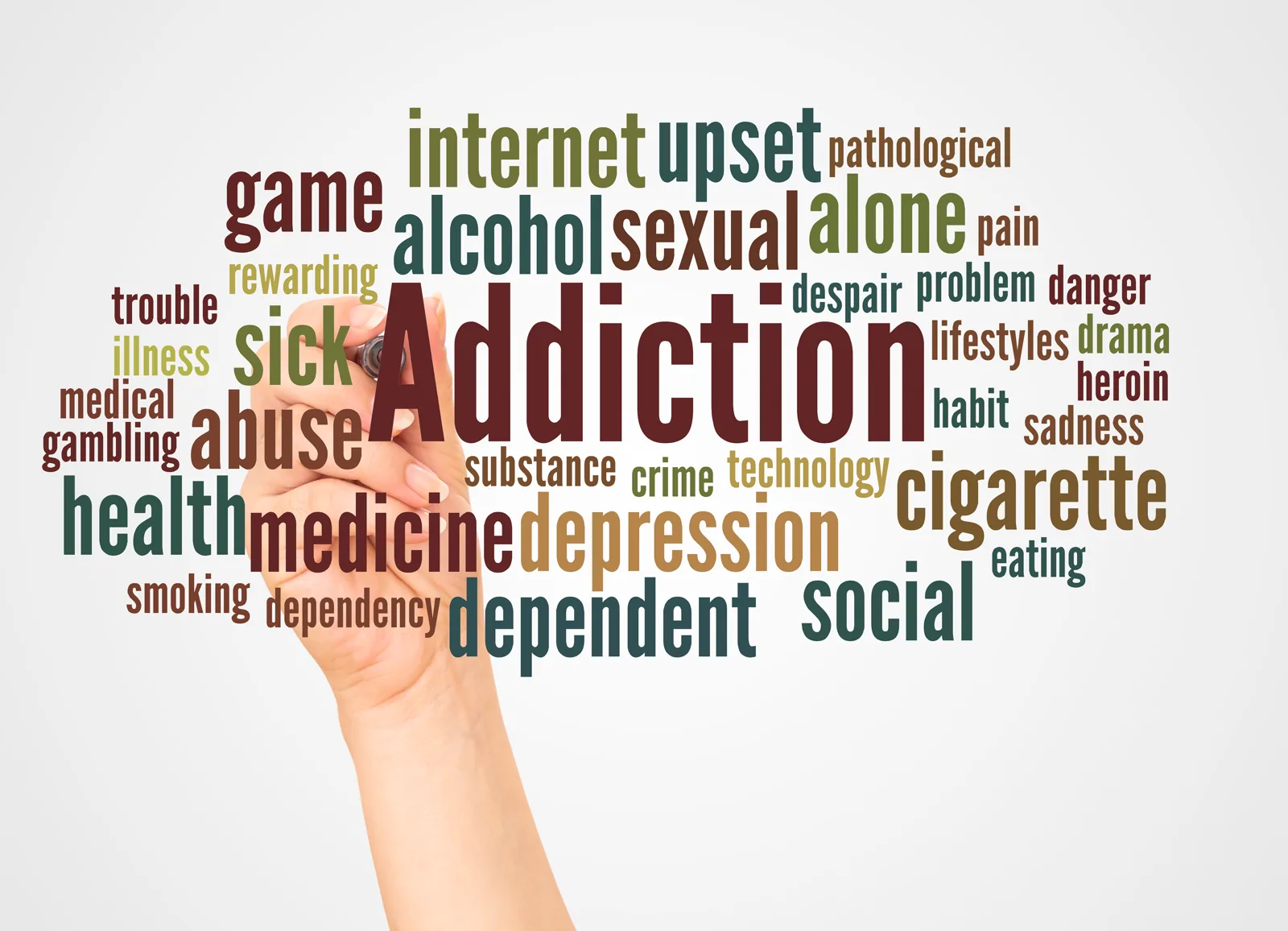 A hand writing the word 'addiction' as part of a conceptual word cloud, warm-toned background