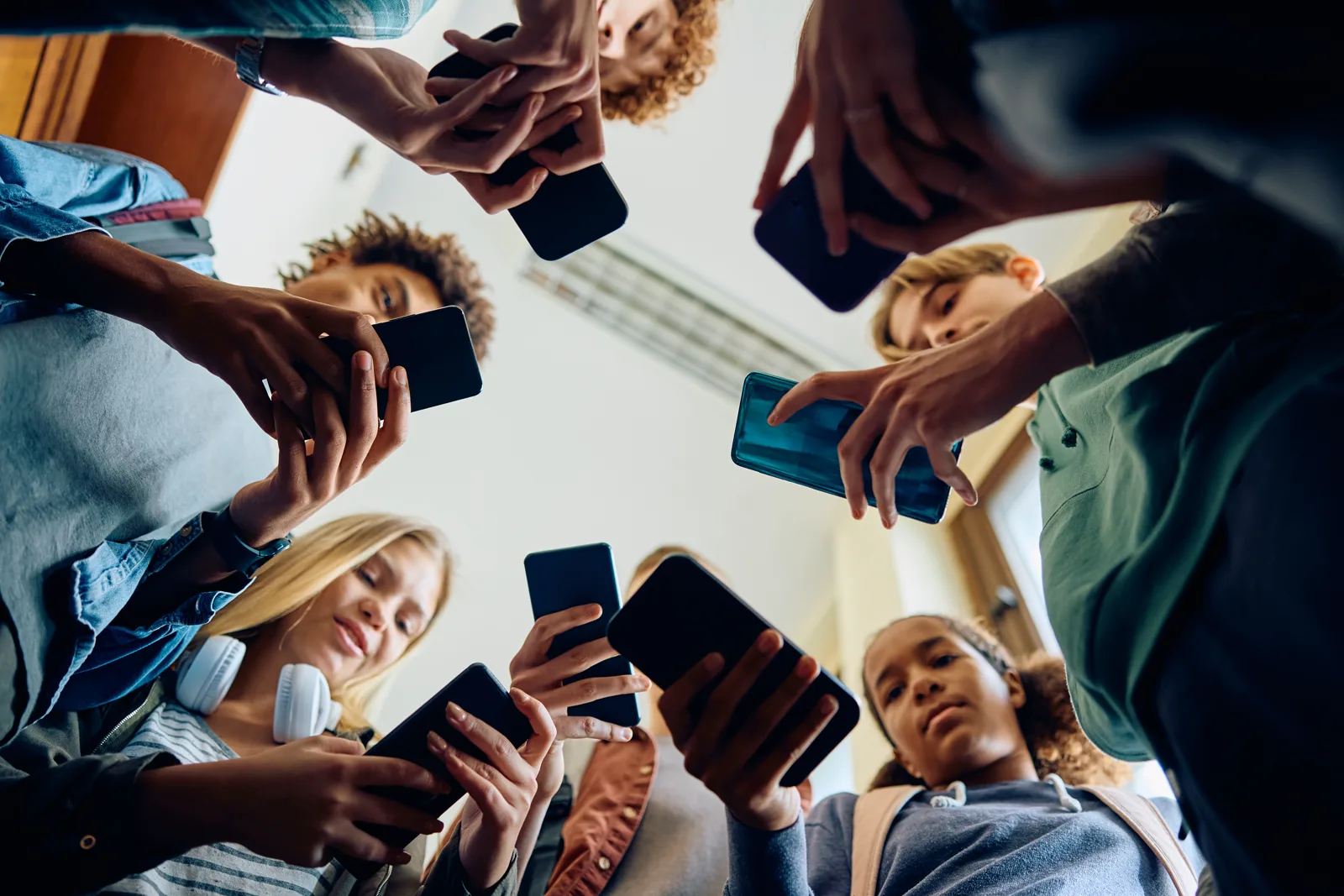 A low-angle view of a group of teenagers looking down at their smartphones